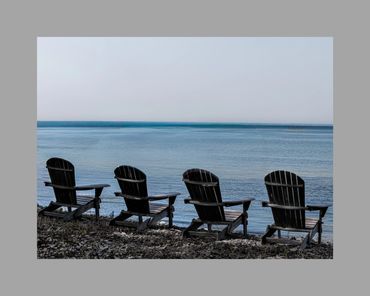 Four wooden chairs facing a calm blue lake under a clear sky.