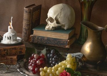 Still life with skull, old books, candle, grapes, and brass pitcher.