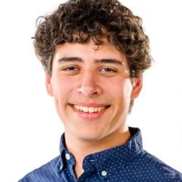 Smiling young man with curly hair in a blue shirt.