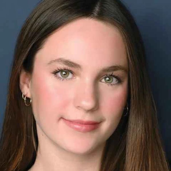 Young woman with long brown hair and green eyes smiles gently.
