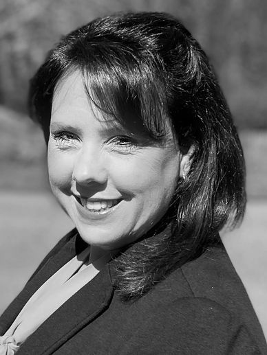 Woman with dark hair smiling in a professional outfit outdoors.