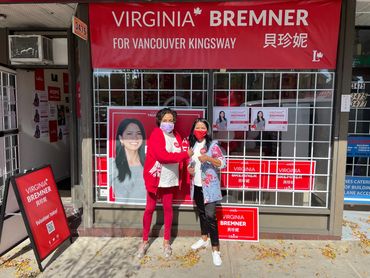 Two women pose in front of a Virginia Bremner campaign office with bright red signs.