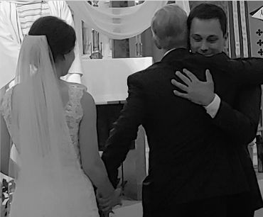 This is an image of the father of the bride hugging the groom while holding his daughter's hand.