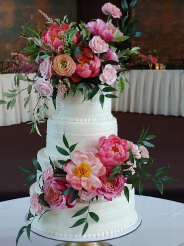 This is a stunning image of a three tiered, white wedding cake. It is covered in real pink flowers.