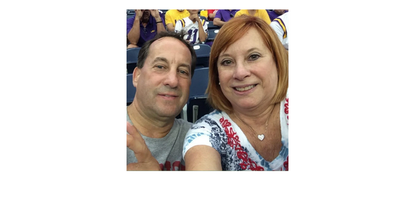 Smiling couple taking a selfie at a sports event with fans in the background.