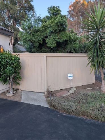 Beige wooden fence with greenery and security sign.