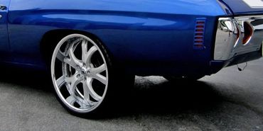 Sleek blue classic muscle car with oversized chrome wheels parked outside.