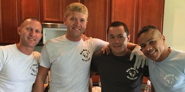 Four men smiling and posing together in a kitchen, wearing matching gloves and cleaning attire.