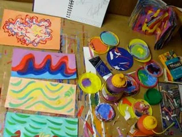 A table with colorful abstract paintings and various paint supplies.