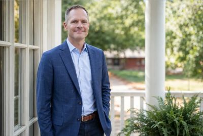 Man in blue blazer standing on porch.