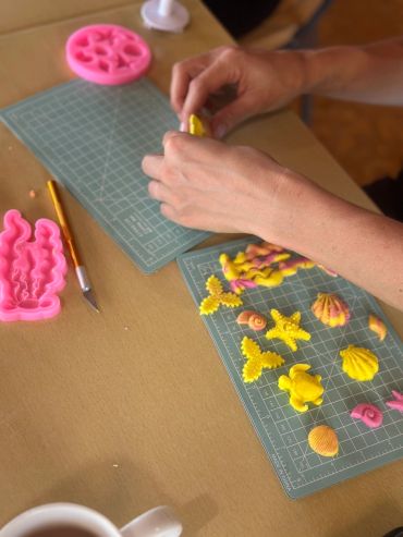 Hands crafting colorful sea-themed clay shapes.