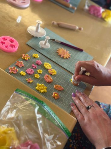 Hands crafting colorful floral decorations with tools on a table.
