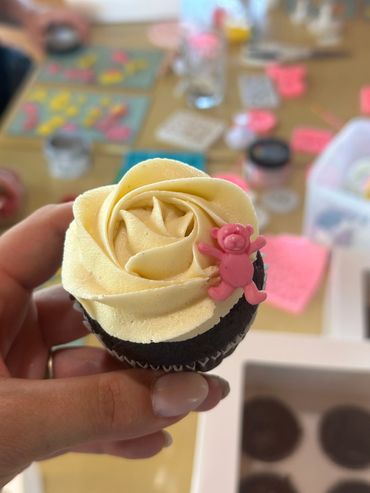 Cupcake with yellow rose frosting and a pink bear decoration.