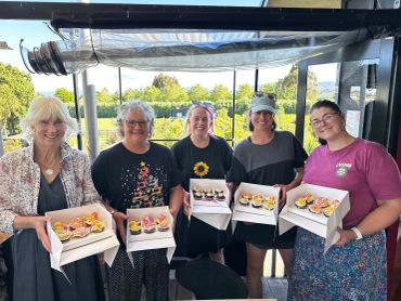 Group of five women holding decorated cupcakes indoors.
