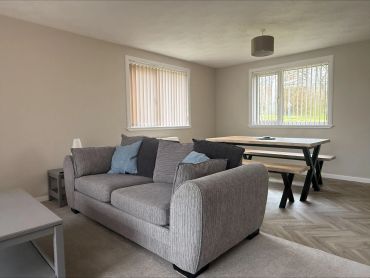 Modern living room with gray sofa and wooden dining table near windows.