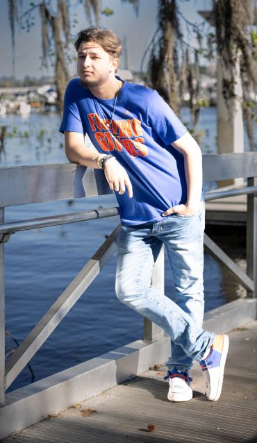 Young man in blue shirt leaning on railing by the water.