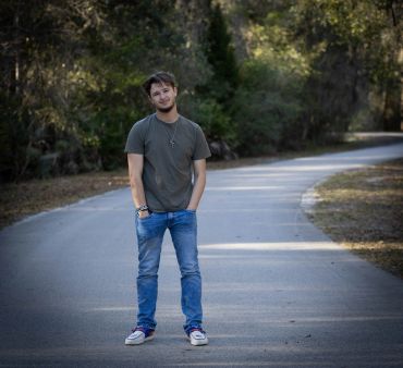 Young man standing on a quiet road surrounded by trees.