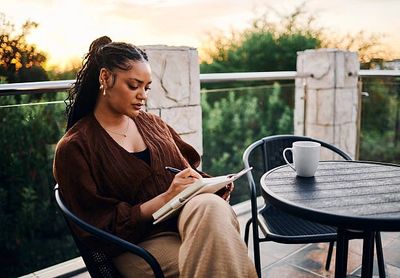 A woman writing in a notebook on a balcony at sunset.