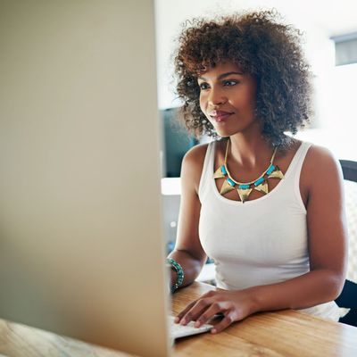 Woman with curly hair working on a computer at a wooden desk.