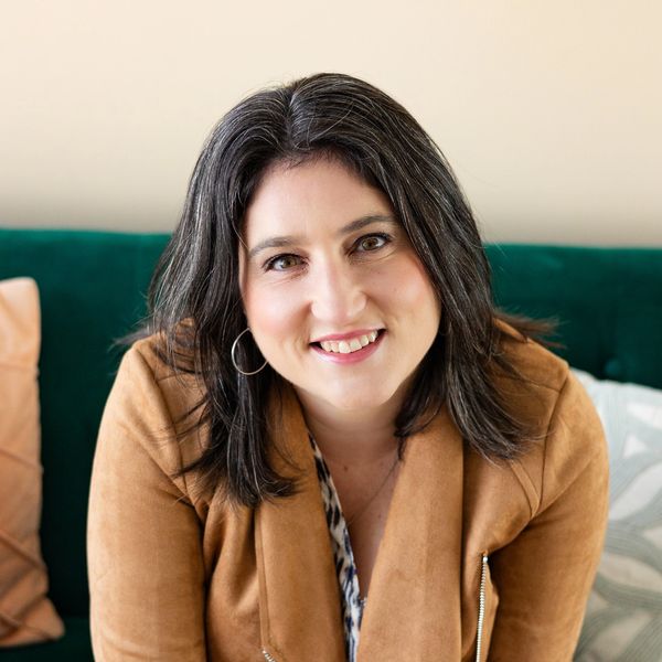 Smiling woman with dark hair wearing a brown jacket on a green couch.