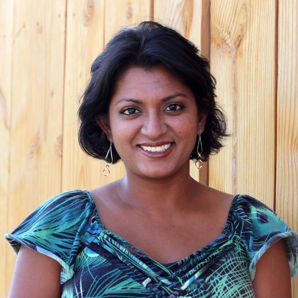 Smiling woman with short hair in a patterned blue and green top against a wooden background.