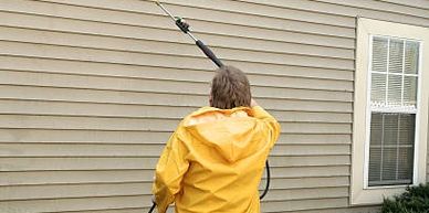 Person in yellow rain gear pressure washing house siding outdoors.