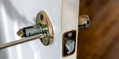 A screwdriver unscrewing a door latch plate on a white door.