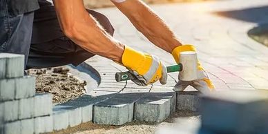 Worker installing paving stones with gloves and hammer at sunset.
