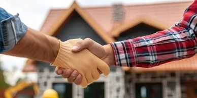 Two people shaking hands in front of a house under construction.