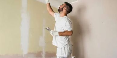 Man repairing ceiling with putty knife in a room under renovation.