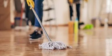 Person mopping a wooden floor wearing yellow gloves indoors.