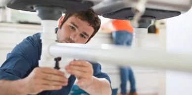 A plumber fixing pipes under a sink indoors.