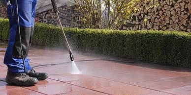 Person pressure washing a tiled patio outdoors.