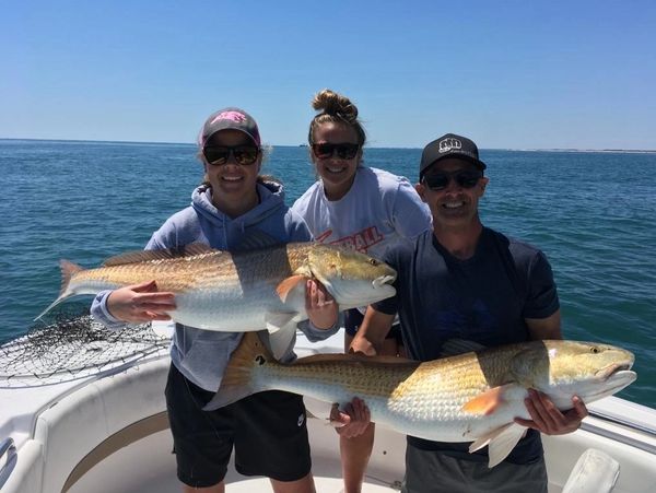 Three people holding large fish on a boat.