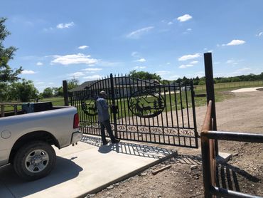 A man standing in front of custom fabricated metal gates at the beginning of a driveway.