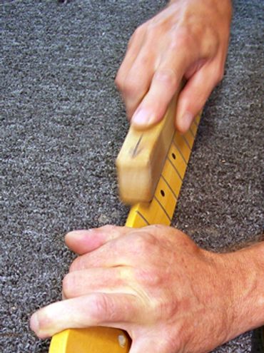 Hands cleaning a guitar neck with a brush.