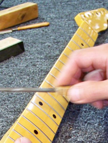 Hand working on a guitar neck with tools around.