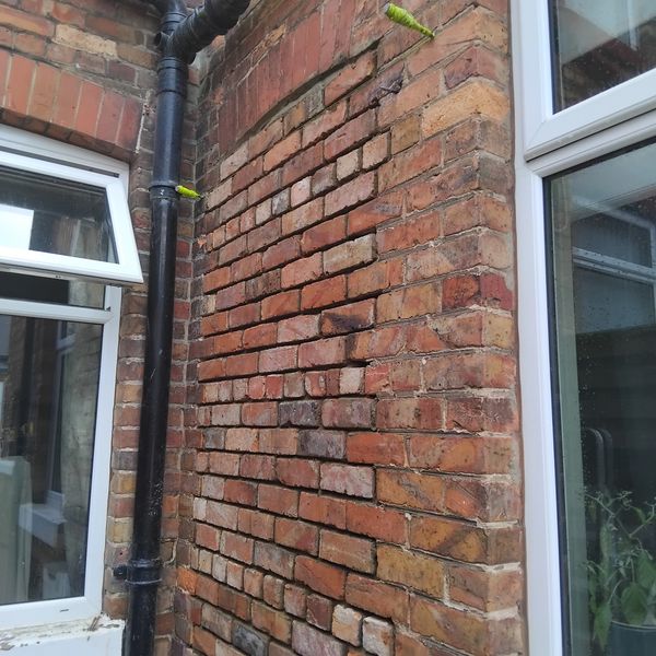 A section of a brick wall with uneven bricks and two white windows.