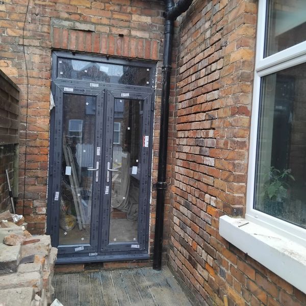 Newly installed black-framed glass door on a brick wall with construction materials around.