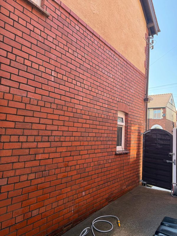 Red brick wall with a small window and partly open black wooden gate.