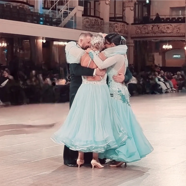Four ballroom dancers embracing in blue dresses and black attire.