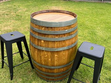 Wooden barrel table with two black metal stools on grass.