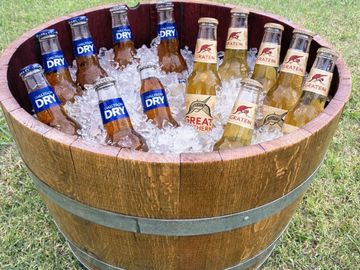 Wooden barrel filled with ice-cold beer bottles outdoors.