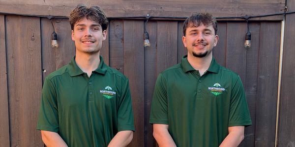 Two young men in green Northbound polo shirts standing against a wooden fence.