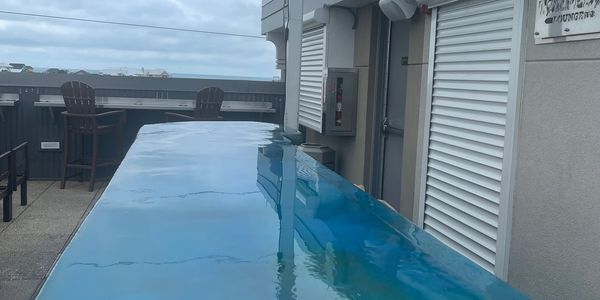 A rooftop pool with clear blue water and outdoor chairs under a cloudy sky.