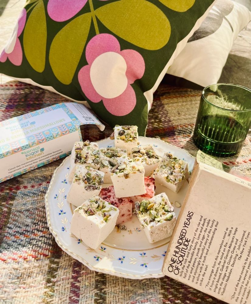 Pistachio marshmallows on a plate with picnic rug, book and cushion and green glass