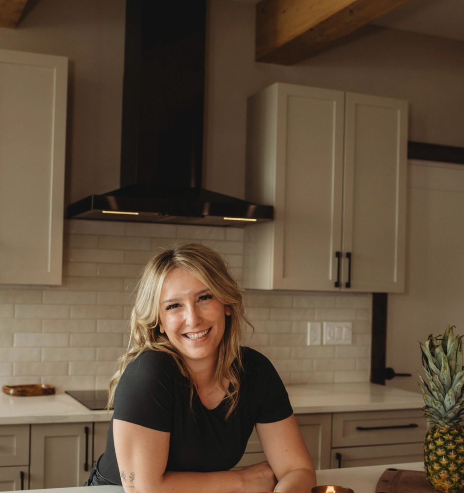Smiling woman leaning on kitchen counter with pineapple nearby.
