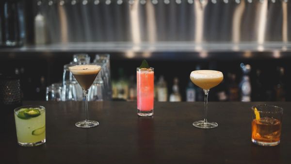 Five colorful cocktails lined up on a bar counter with a blurred background.