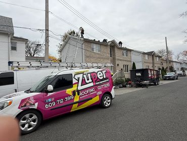 Roofers working on a residential building with a Zuper Roofing & Gutters van parked nearby.