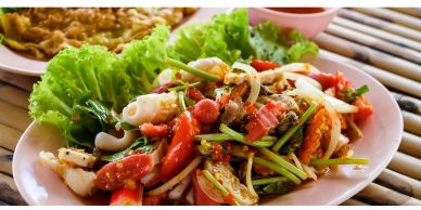 A colorful Thai seafood salad with fresh vegetables on a white plate.